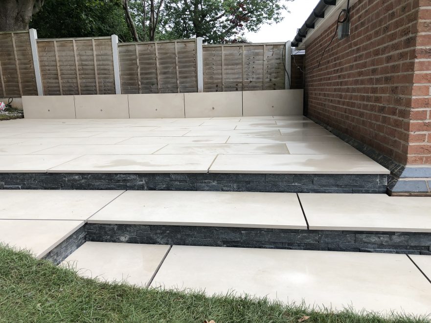 50m² porcelain patio with split-face granite wall, sleeper planters and lighting, Stone