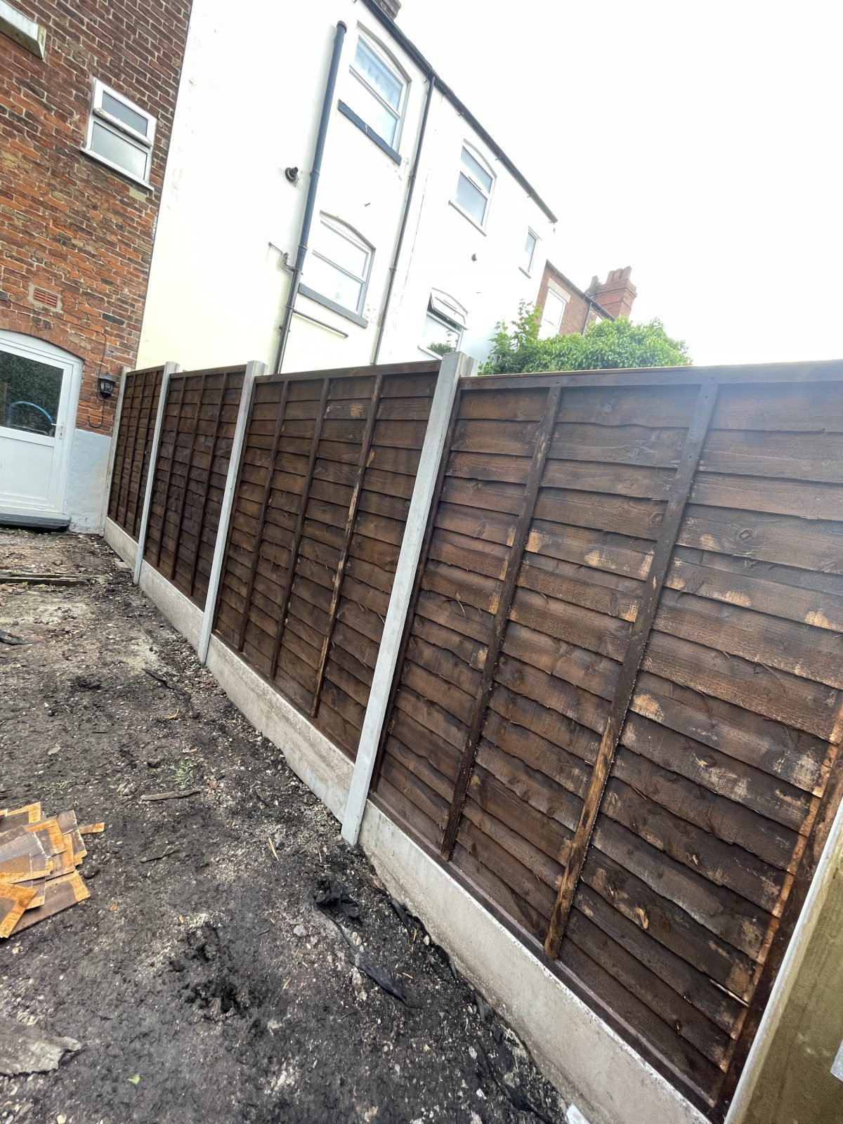 Dark brown lap fence panels on concrete posts and gravel boards with a new gate, Stone, Staffordshire
