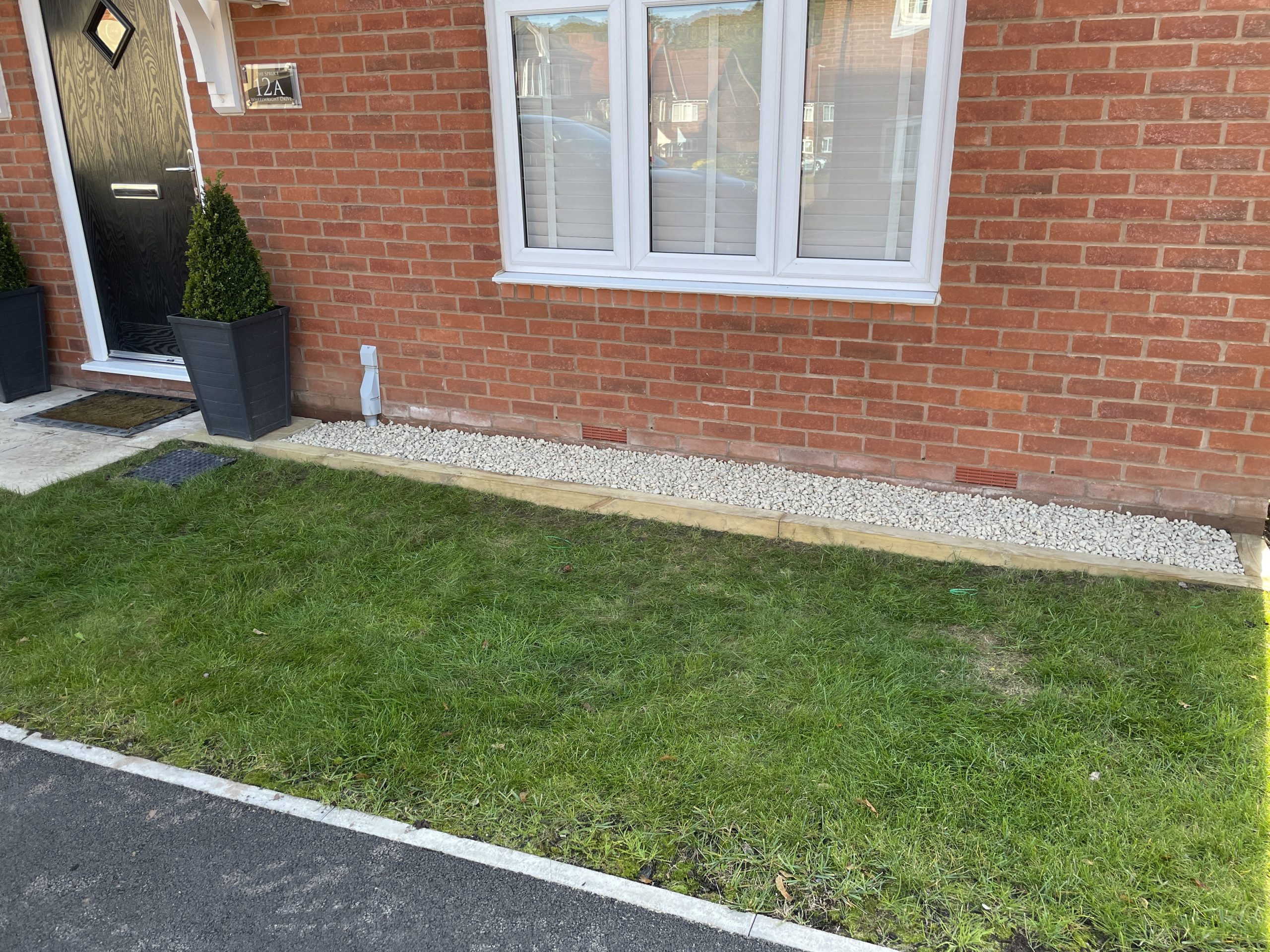 Low timber sleeper borders filled with white decorative stone either side of a front door step, Stone